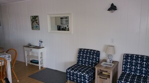 A room with a white wall, a wooden chair, a small table with a lamp, and a sofa with a nautical pattern. - OC Md family condo, 19th bdwlk- Sleeps 8, 3 bedroom, 2 bath, Positive reviews. (Ocean City)