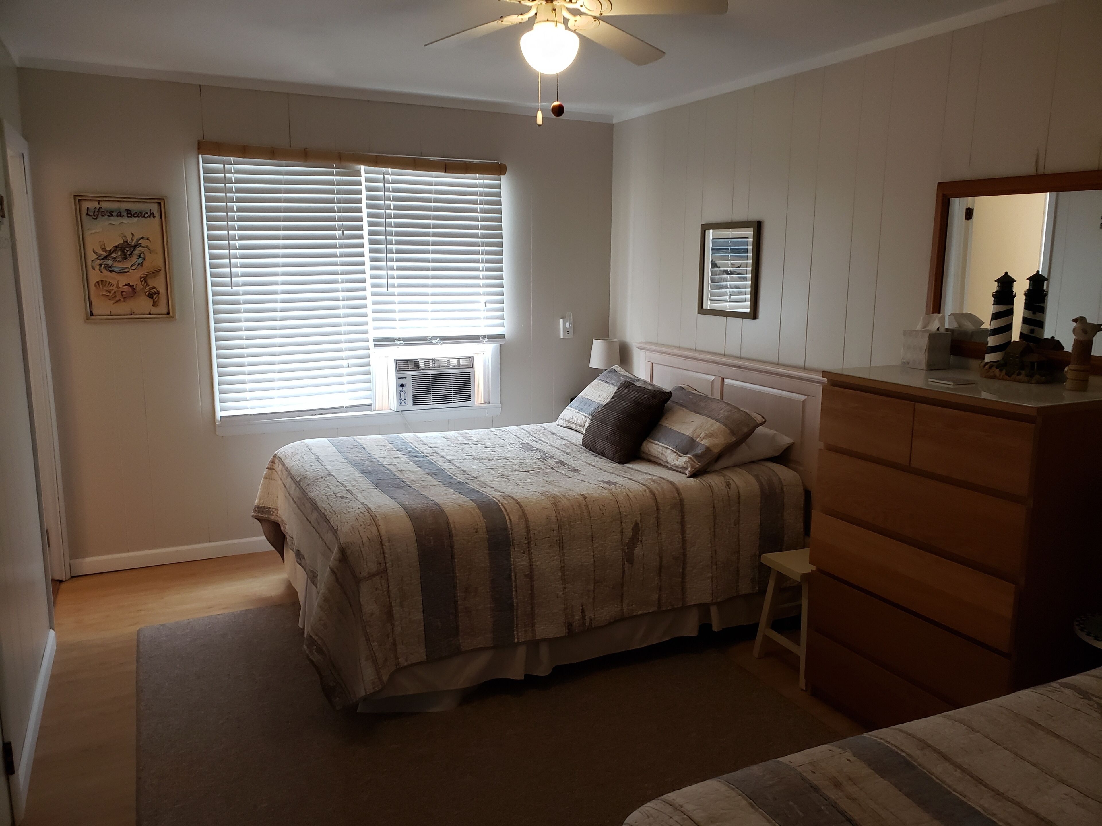 Une chambre à coucher comprenant un lit, une commode, une fenêtre avec des stores et un ventilateur de plafond.
