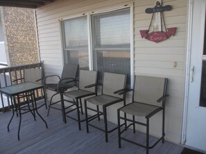 A covered outdoor seating area with four chairs and a table, a welcome sign, and a view through the window. - OC Md family condo, 19th bdwlk- Sleeps 8, 3 bedroom, 2 bath, Positive reviews. (Ocean City)