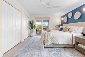 A bedroom with a bed, bedside tables, a ceiling fan, a large window, and a view of the outdoors. - Rod and Reel Haven on Minnow Creek (Hernando Beach)
