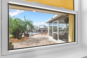 A view through a window of a patio area with a boat dock, palm trees, and a seating area with chairs and a table. - Rod and Reel Haven on Minnow Creek (Hernando Beach)