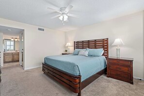 Ein Schlafzimmer mit Bett, Nachttischen, Kommode, Deckenventilator und angrenzendem Badezimmer.