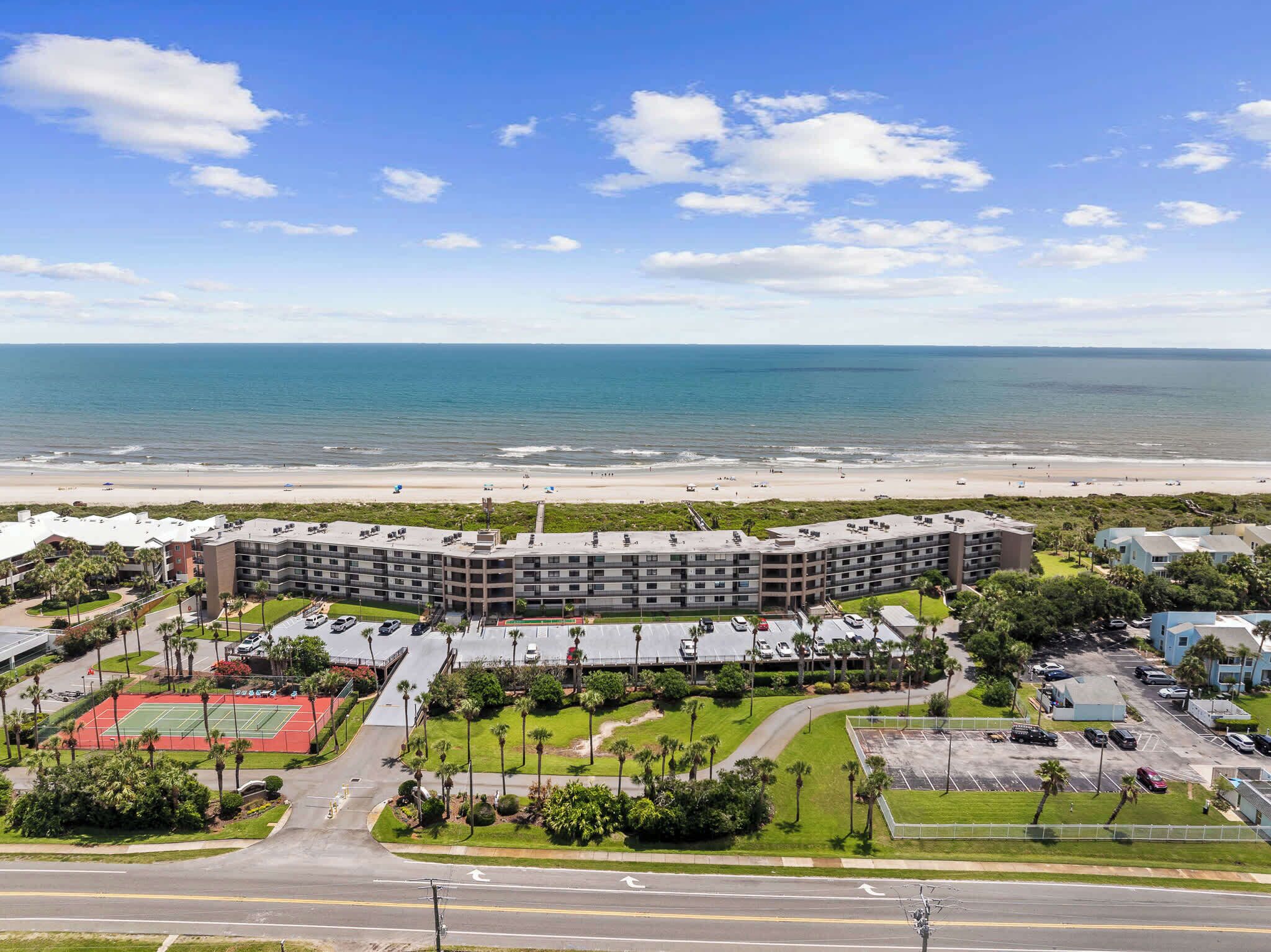 A beachfront hotel with multiple floors, a parking lot, and a tennis court.
