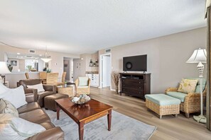 Uma sala de estar com sofá, cadeiras, mesa de centro, televisão e luminária.