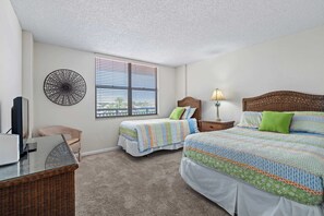 A bedroom with two beds, a television, a lamp, and a wicker chair. - Sandy Toes l Oceanfront Condo l Heated Pool (St. Augustine)