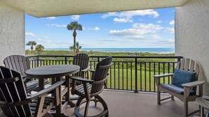 A balcony with a view of the ocean, furnished with wooden chairs and a table. - Sandy Toes l Oceanfront Condo l Heated Pool (St. Augustine)
