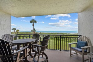 A balcony with a view of the ocean, furnished with wooden chairs and a table. - Sandy Toes l Oceanfront Condo l Heated Pool (St. Augustine)