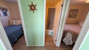 Ein Zimmer mit zwei Betten, einer Tür mit Schiffslrad-Verzierung und einem kleinen, angrenzenden Badezimmer.