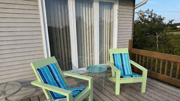 Eine Terrasse mit zwei Stühlen, einem kleinen Tisch, einer Schiebetür aus Glas und einem Holzaushang.