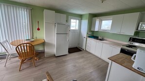 Eine kleine Küche mit weißen Schränken, einem Holztisch und Meerblick durch ein Fenster.