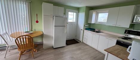 Cocina compacta con armarios blancos, una mesa de comedor de madera y vistas al mar a través de una ventana.