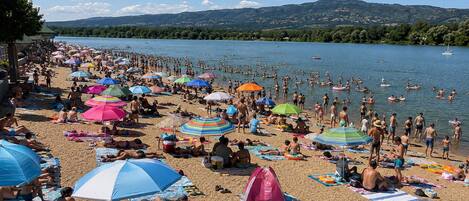 Ein belebter Strand mit Menschen, die sich sonnen und schwimmen, umgeben von einem See und Hügeln.