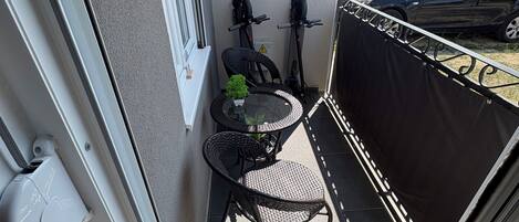 A small balcony with a table and chairs, a scooter, and a car parked outside.