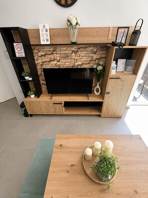 En moderne stue med en stenvæg, et fladskærms-tv og et træbord med stearinlys og planter.