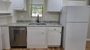 Uma cozinha com armários brancos, lava-louças em aço inoxidável, uma pia dupla e geladeira branca.