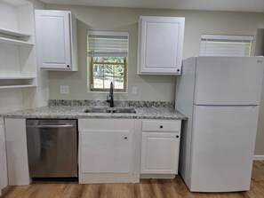 Una cocina con armarios blancos, lavavajillas de acero inoxidable, un lavamanos doble y un refrigerador blanco.