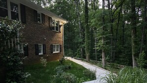 Uma casa de dois andares de tijolo, com entrada pavimentada e gramado bem cuidado.