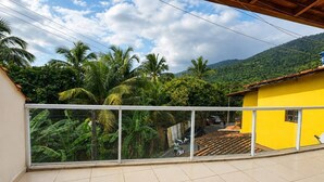 Ein Balkon mit Blick auf ein gelbes Gebäude, Palmen und eine hügelige Landschaft.
