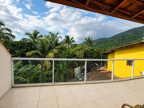 Un balcón con vistas a un edificio amarillo, palmeras y un paisaje montañoso.