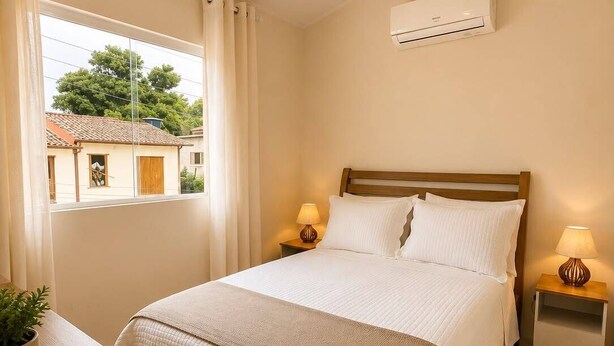 Ein Schlafzimmer mit einem Bett, Nachttischlampen, einer Topfpflanze und einem Fenster mit Vorhängen.