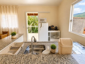 A kitchen with granite countertops, a stainless steel sink, a microwave, and a window with a view of greenery. - House with ocean view, Ilhabela/SP (Ilhabela)
