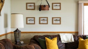 A living room with a brown leather sofa, a lamp, and framed fish illustrations on the wall. - Lakefront, 5BR Home w/Sandy Beach, Dock & Kayaks (Excelsior Township)