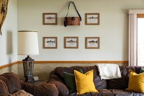 A living room with a brown leather sofa, a lamp, and framed fish illustrations on the wall. - Lakefront, 5BR Home w/Sandy Beach, Dock & Kayaks (Excelsior Township)