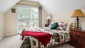 A bedroom with a large window, a bed with a quilt, a nightstand, a lamp, and a ceiling fan. - Lakefront, 5BR Home w/Sandy Beach, Dock & Kayaks (Excelsior Township)
