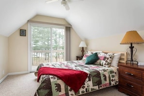 A bedroom with a large window, a bed with a quilt, a nightstand, a lamp, and a ceiling fan. - Lakefront, 5BR Home w/Sandy Beach, Dock & Kayaks (Excelsior Township)