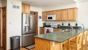 A modern kitchen with wooden cabinets, stainless steel appliances, and a granite countertop. - Lakefront, 5BR Home w/Sandy Beach, Dock & Kayaks (Excelsior Township)