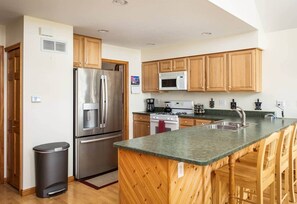 A modern kitchen with wooden cabinets, stainless steel appliances, and a granite countertop. - Lakefront, 5BR Home w/Sandy Beach, Dock & Kayaks (Excelsior Township)