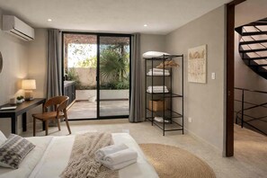 A hotel room with a bed, a desk with a chair, a black metal shelf with towels, a window with curtains, and a spiral staircase. - House in Centro: Pool, Garden, Terrace, and Rooftop (Mérida)