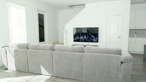 A modern living room with a grey sectional sofa, a flat-screen TV, and a staircase leading to a kitchen area. - Spacious 4-bedroom Townhome with AC in enchanting Davenport near Disney (Davenport)