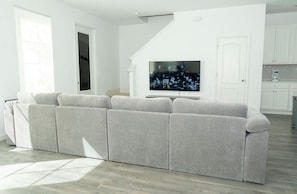Ein modernes Wohnzimmer mit einem grauen Ecksofa, einem Flachbildfernseher und einer Treppe zu einer Küchenzeile.