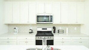 A kitchen with white cabinets, a microwave, a stove, a coffee maker, and a toaster. - Spacious 4-bedroom Townhome with AC in enchanting Davenport near Disney (Davenport)