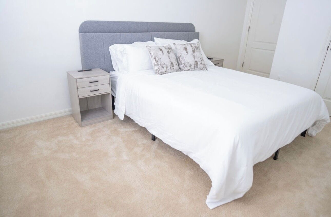 Un dormitorio con cama, mesitas de noche y piso alfombrado.