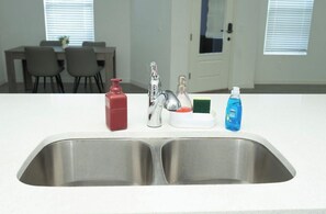 A kitchen with a double sink, a red soap dispenser, a silver faucet, a green sponge, and a blue dish soap bottle. - Spacious 4-bedroom Townhome with AC in enchanting Davenport near Disney (Davenport)