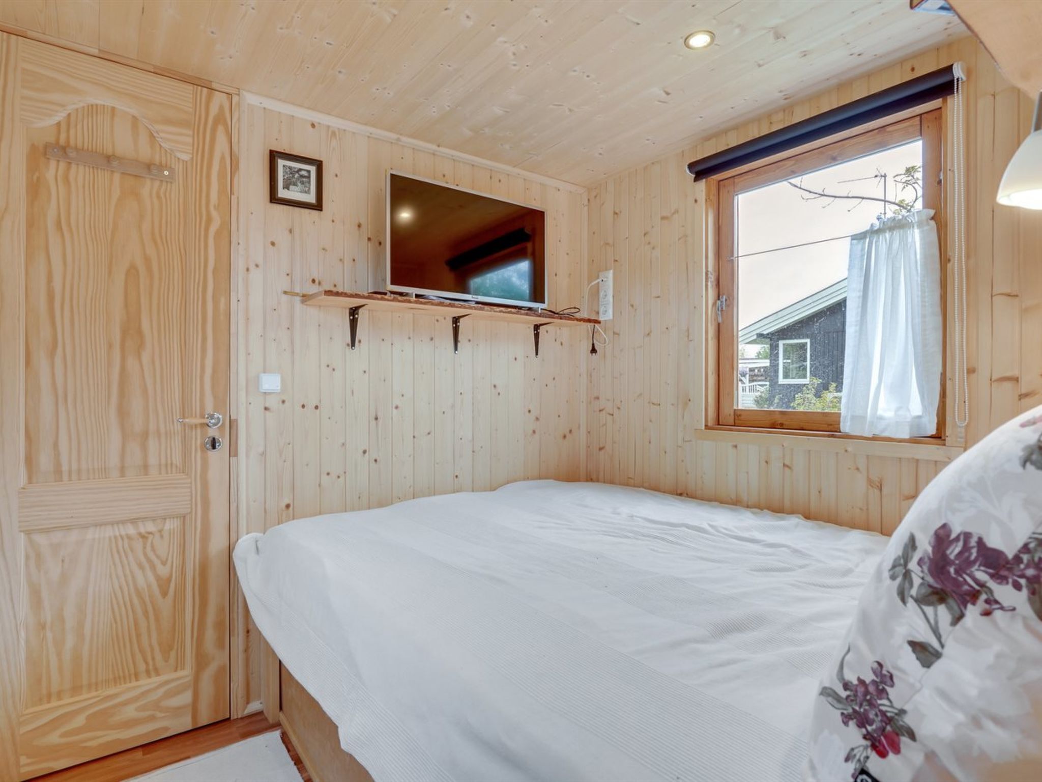 Een kamer met houten lambrisering, een bed, een wandtelevisie en een raam met gordijnen.