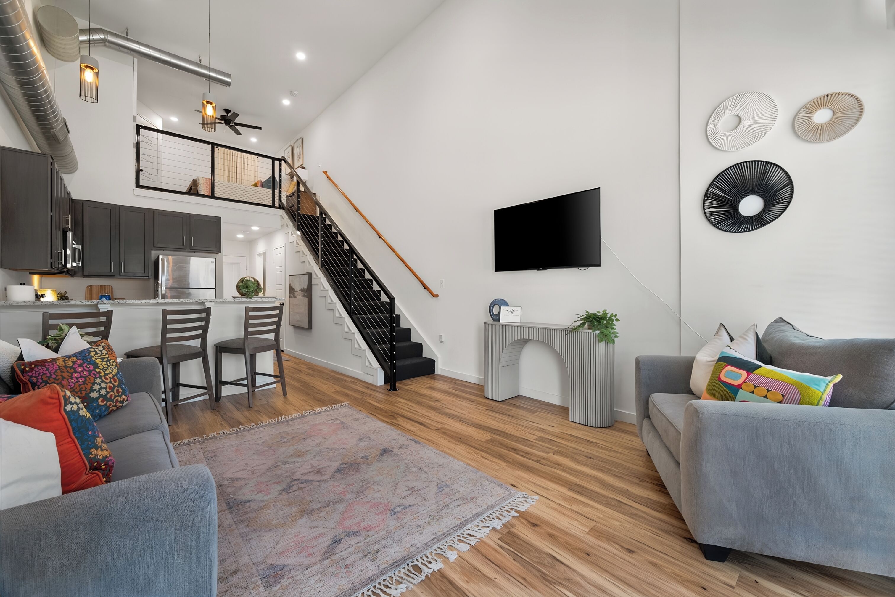 A modern living space with a kitchen, dining area, and a staircase leading to an upper level.
