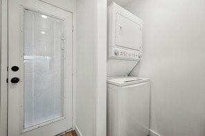 A compact laundry room with a white washing machine and dryer stacked vertically. - Red Raider Loft (Lubbock)