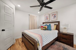 A bedroom with a bed, nightstands, a ceiling fan, a door, and two framed pictures on the wall. - Red Raider Loft (Lubbock)