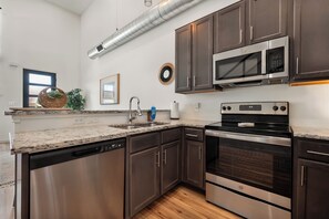 A modern kitchen with stainless steel appliances, dark wooden cabinets, and a granite countertop. - Red Raider Loft (Lubbock)