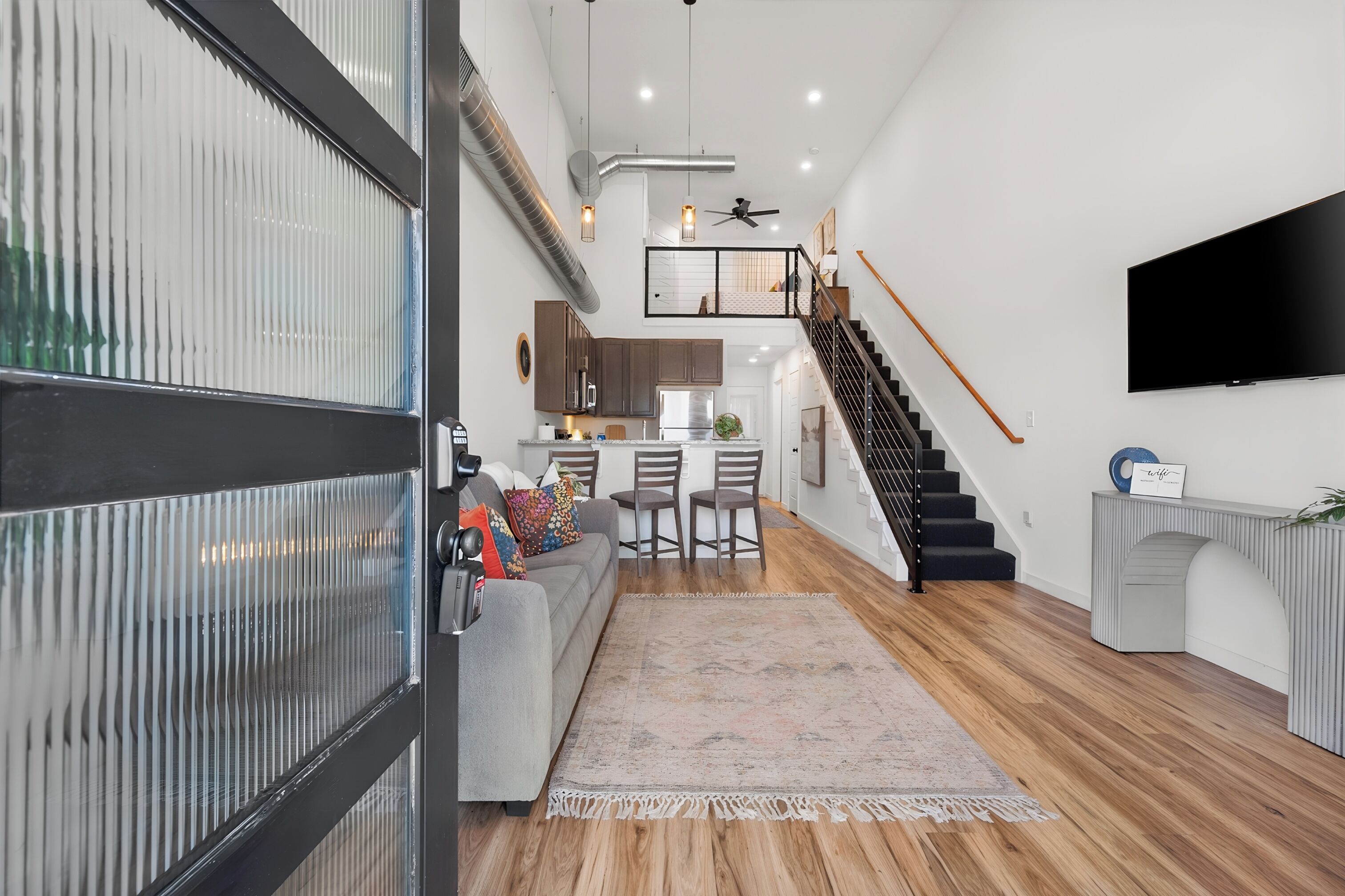 A modern interior with a staircase, a flat-screen TV, and a kitchen area.
