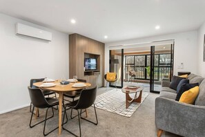 A modern living room with a dining area, a sofa, a TV, and a large window. - Modern Townhouse  Walk to Hagley Park & Hospital (Christchurch)