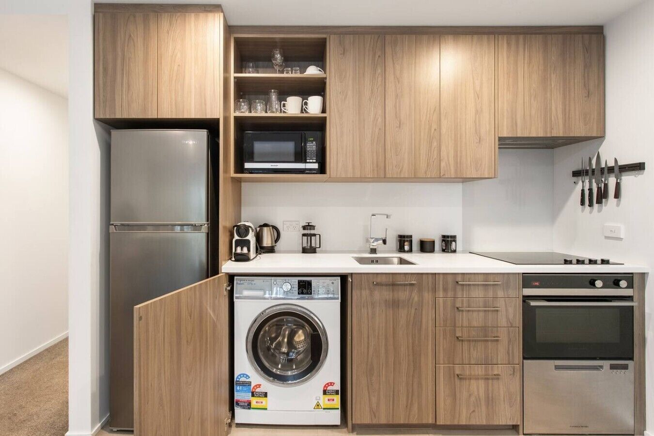Una cocina compacta con lavadora integrada, microondas, cocina y muebles de madera.