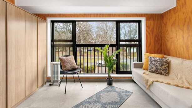 A modern living room with a large window, a sofa, a chair, and a potted plant. - Modern Townhouse  Walk to Hagley Park & Hospital (Christchurch)