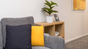A grey sofa with a dark and a yellow pillow, a white potted plant, and a wooden side table with bowls. - Modern Townhouse  Walk to Hagley Park & Hospital (Christchurch)