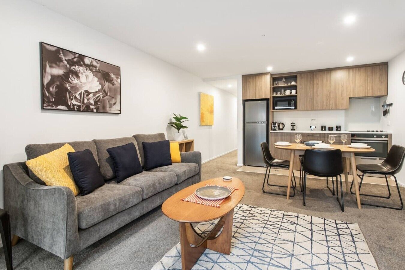 Una sala de estar moderna con un sofá gris, una mesa de centro de madera y un comedor con una pequeña mesa y sillas.