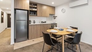 A compact kitchen with a refrigerator, microwave, and stove, a dining table with chairs, and a clock on the wall. - Modern Townhouse  Walk to Hagley Park & Hospital (Christchurch)