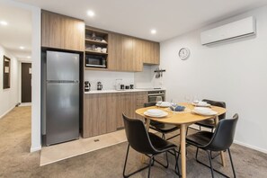 Eine kleine Küche mit Kühlschrank, Mikrowelle und Herd, ein Esstisch mit Stühlen und eine Uhr an der Wand.